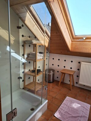 Un cerramiento de ducha con puertas de cristal, un estante de madera y un taburete pequeño.