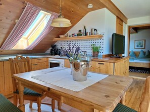 Una cocina acogedora con armarios de madera, una mesa de comedor con un florero y un televisor al fondo.