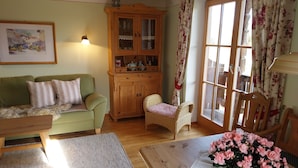 A cozy living room with a green sofa, a wooden cabinet, a wicker chair, and a table with a floral centerpiece. - Heissbauer Vacation Rental "Karwendelblick" with Mountain Views, 2 Bedrooms, and 2 Bathrooms (Wackersberg)