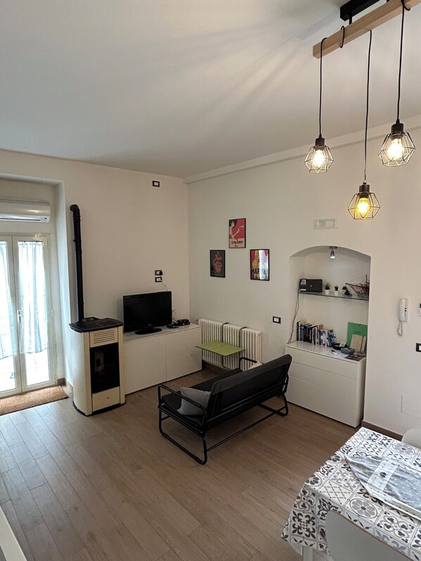 Ein kompakter Wohnraum mit Fernseher, Heizkörper, einer Bank und einem kleinen Tisch mit gefliestem Tischläufer.