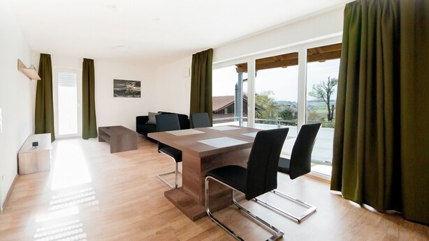 A modern dining area with a wooden table, black chairs, and a view of the outdoors. - 5 large apartments, for a maximum of 4 people in an idyllic location near Munich (Billingsdorf)