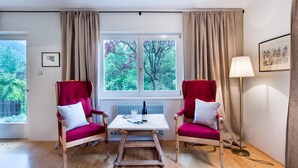 Ein Zimmer mit zwei roten Sesseln, einem Holztisch, einem Fenster mit Blick auf Bäume und einer Lampe.