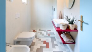 Ein modernes Badezimmer mit einer Bidet-Funktion, Toilette und Dusche. Ein rotes Regal zeigt Handtücher und einen Topfpflanzen.