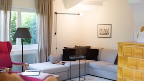 Ein modernes Wohnzimmer mit einer Eckcouch, einem roten Sessel, einem kleinen runden Tisch und einer Stehlampe.