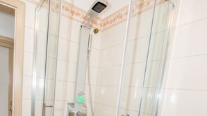 Une cabine de douche fermée par des parois en verre, avec un pommeau de douche à main, une serviette sur le sol et des toilettes sur la droite.