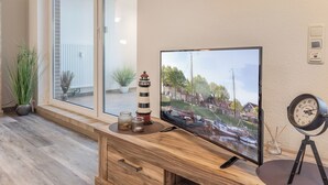Ein Holztisch mit einem Flachbildfernseher, der eine schöne Aussicht zeigt, einem kleinen Leuchtturm-Modell und einer Uhr auf einem Stativ.