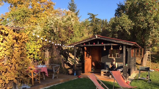 Eine rustikale Holzhütte mit rotem Dach, einer Veranda mit Tisch und Stühlen und einer Rutsche.