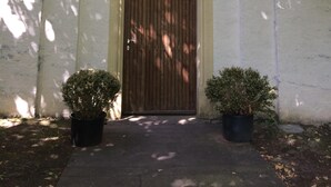 A church entrance with a wooden door, an arched doorway, and a cross above. There are two potted plants on either side of the door. - Old forge in a listed courtyard (Messerich)