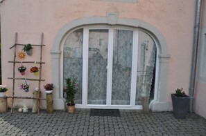 A building entrance with a large arched door, a wooden ladder with potted plants, and a cobblestone pavement. - Old forge in a listed courtyard (Messerich)