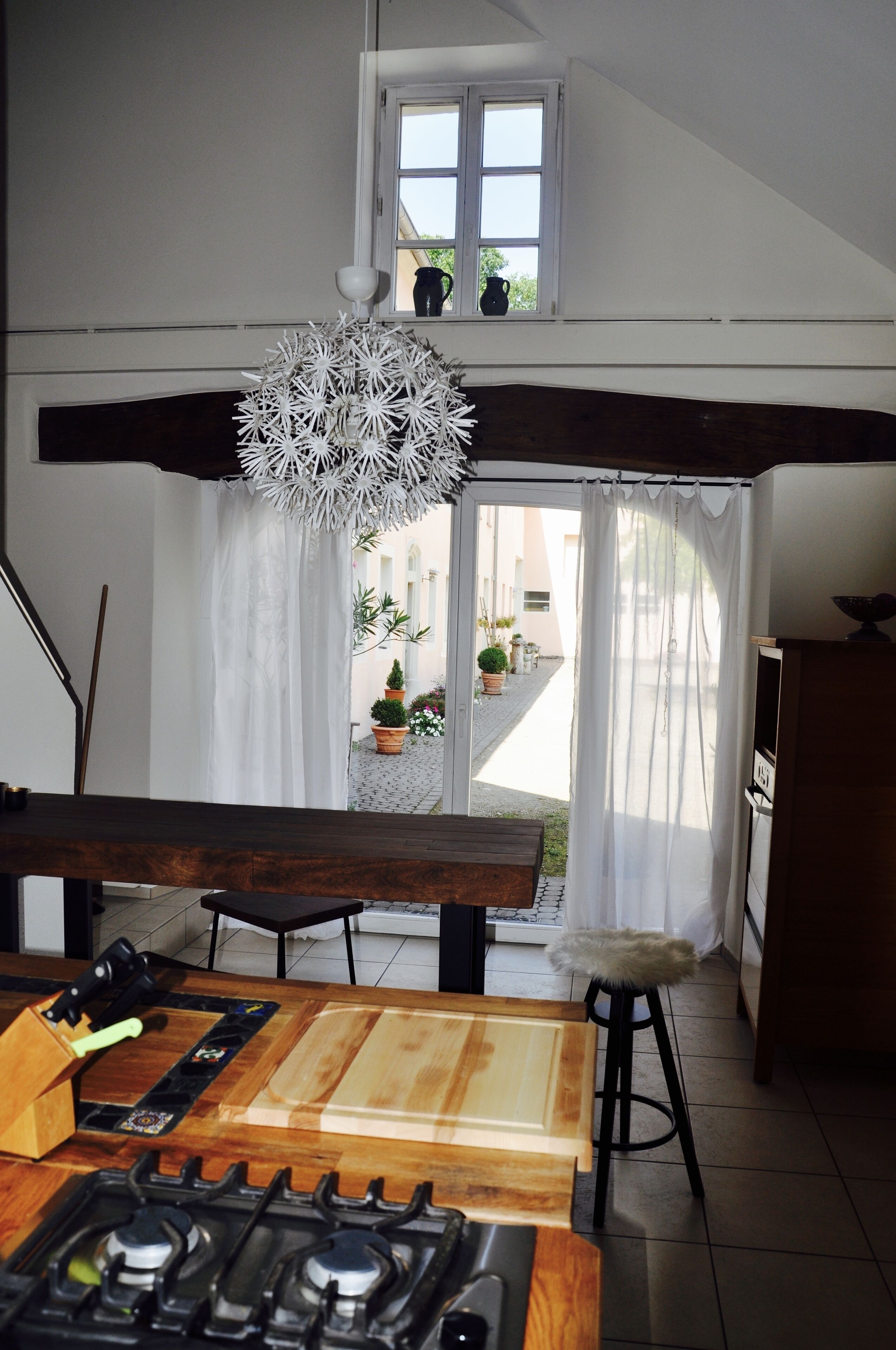 A kitchen with a wooden table, a gas stove, and a window overlooking a garden.