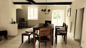 A dining area with a wooden table and chairs, a chandelier, and a view of the outdoors through a window. - Old forge in a listed courtyard (Messerich)
