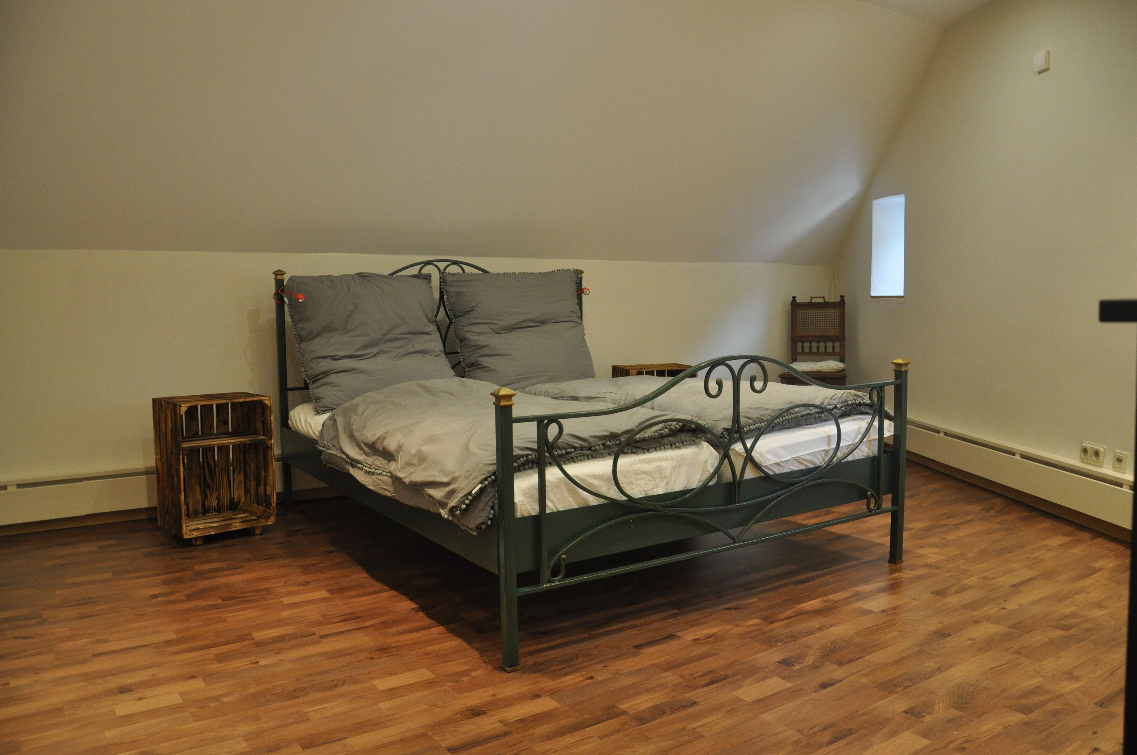 Una cama individual con estructura metálica en una habitación con suelo de madera y techo inclinado.