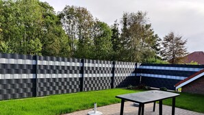 A modern outdoor patio with a black and white patterned fence, a round table, and a brick pathway. - Super idyllic vacation home with privacy to relax, WiFi included. (Jemgum)