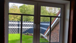 A window with a view of a brick wall and a grassy yard. - Super idyllic vacation home with privacy to relax, WiFi included. (Jemgum)