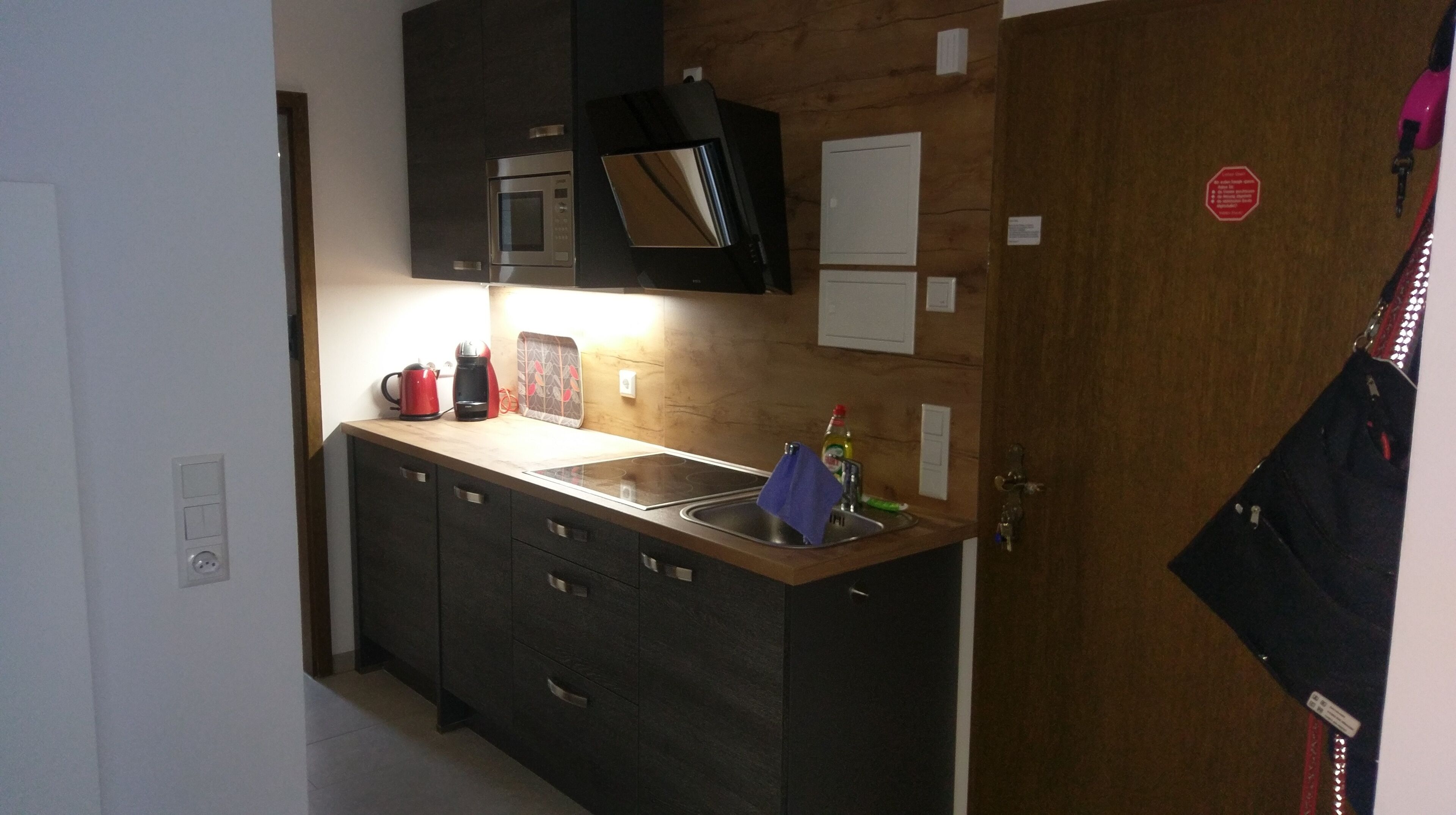 A compact kitchen with dark cabinets, a microwave, a kettle, and a sink.