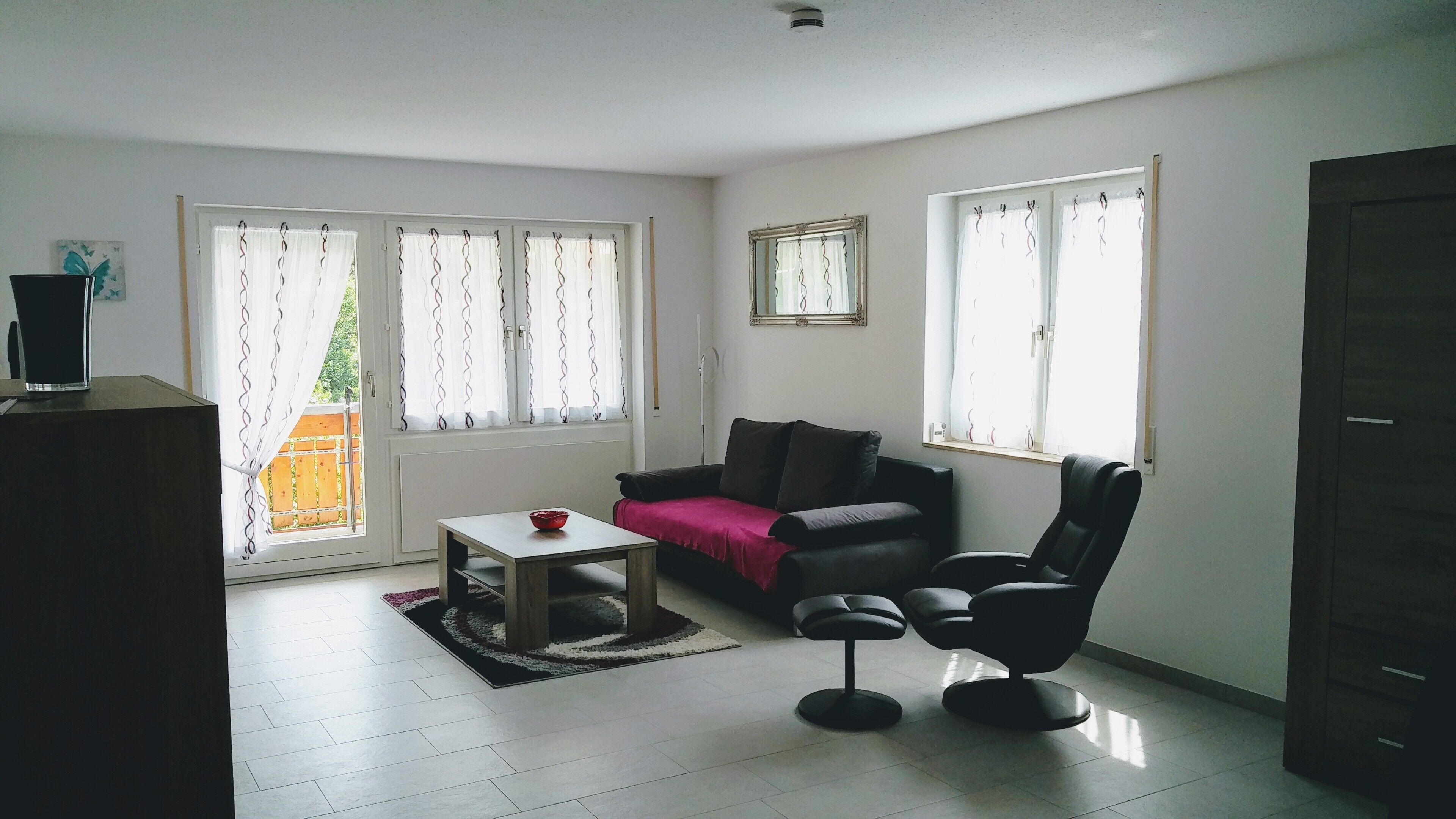 A living room with a sofa, a coffee table, a chair, and two windows with curtains.