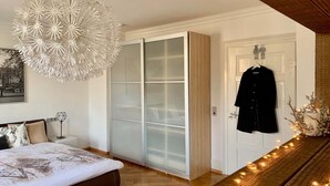 A bedroom with a bed, a white wardrobe, a hanging coat, and a decorative light fixture. - Villa Landenberger Metzingen near Outlet City Apartment Annemarie (Metzingen)