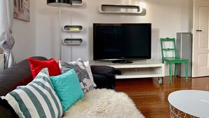 A living room with a flat-screen TV, a white console table, a green chair, and a fluffy white rug. - Villa Landenberger Metzingen near Outlet City Apartment Annemarie (Metzingen)
