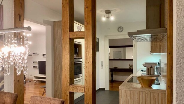 A modern kitchen with wooden accents, a dining area with a chandelier, and a visible kitchen counter. - Villa Landenberger Metzingen near Outlet City Apartment Annemarie (Metzingen)