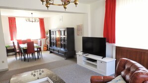 Una sala de estar con televisión, sofá de cuero, mesa de comedor, sillas y estantería.