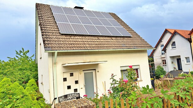 Una casa con techo de paneles solares, una puerta y un pequeño jardín con plantas y una cerca de madera.
