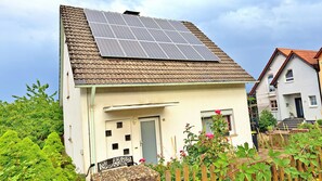 A house with a solar panel roof, a door, and a small garden with plants and a wooden fence. - Family vacation home with garden on the edge of the village; children and dogs welcome (Kalbach-Heubach)