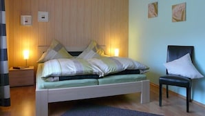 Une chambre bien rangée, avec un lit, des tables de chevet, une chaise et des lampes fixées au mur.