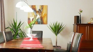 Un coin repas avec une table en bois, des chaises noires, un set de table rouge et deux plantes en pot.