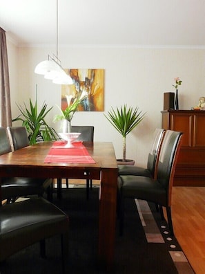 A dining area with a table and chairs, featuring a painting above and a lamp above the table.