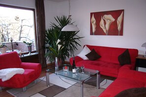 Relax in this stylish living room with a sofa, armchair, and coffee table, surrounded by a large potted plant and a beautiful painting.