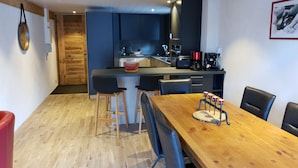 A modern kitchen with dark blue cabinets, a wooden dining table, and a red coffee machine. - Châtel Portes du Soleil Free MultiPass 3-Star Apartment PDS Chairlifts 400 meters away (châtel)