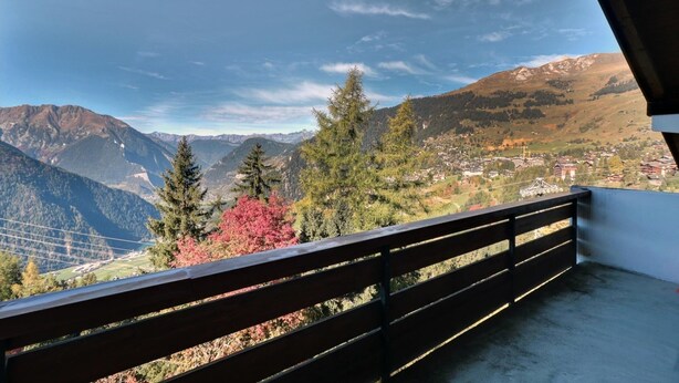 Un balcón con vistas a un paisaje montañoso, que incluye un pueblo y una línea eléctrica.