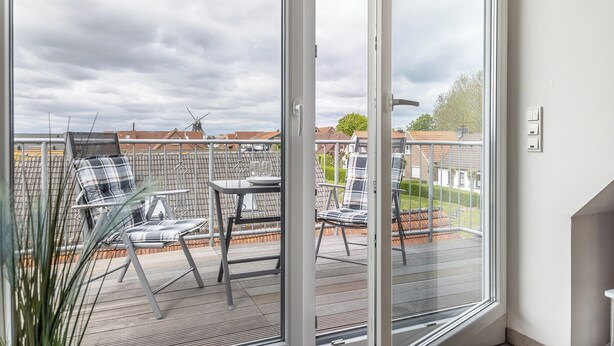 Een balkon met buitenmeubilair, een tafel en uitzicht op een windmolen en huizen.