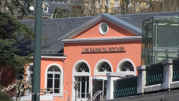 A building with a red facade, arched windows, and a sign reading 'LES BAINS DU ROCHER'.