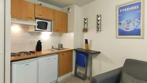 A compact kitchen with wooden cabinets, a microwave, a dishwasher, a sink, and a blue chair.