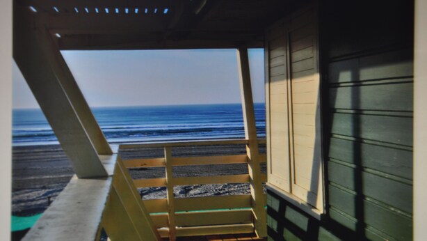 A view from a covered area with a wooden bench, overlooking the beach and ocean.
