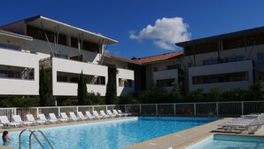 A swimming pool with white lounge chairs and a white fence.