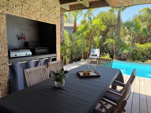 An outdoor dining area with a grill, poolside seating, and lush greenery.