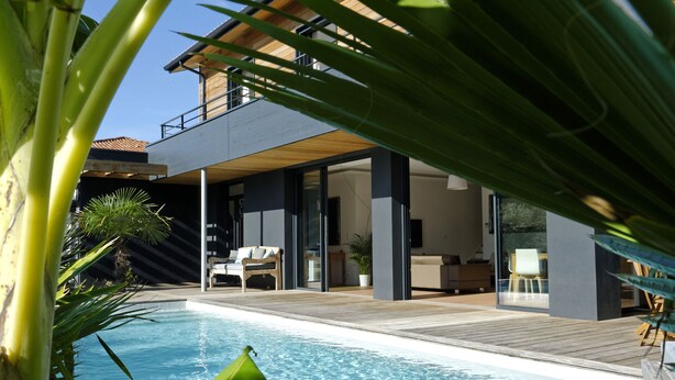 Una casa moderna amb piscina, terrassa de fusta i mobles d'exterior.