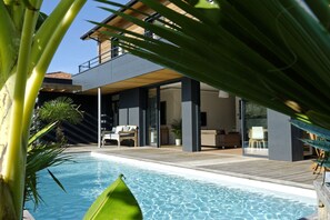 Uma casa moderna com piscina, deck de madeira e mobiliário para área externa.