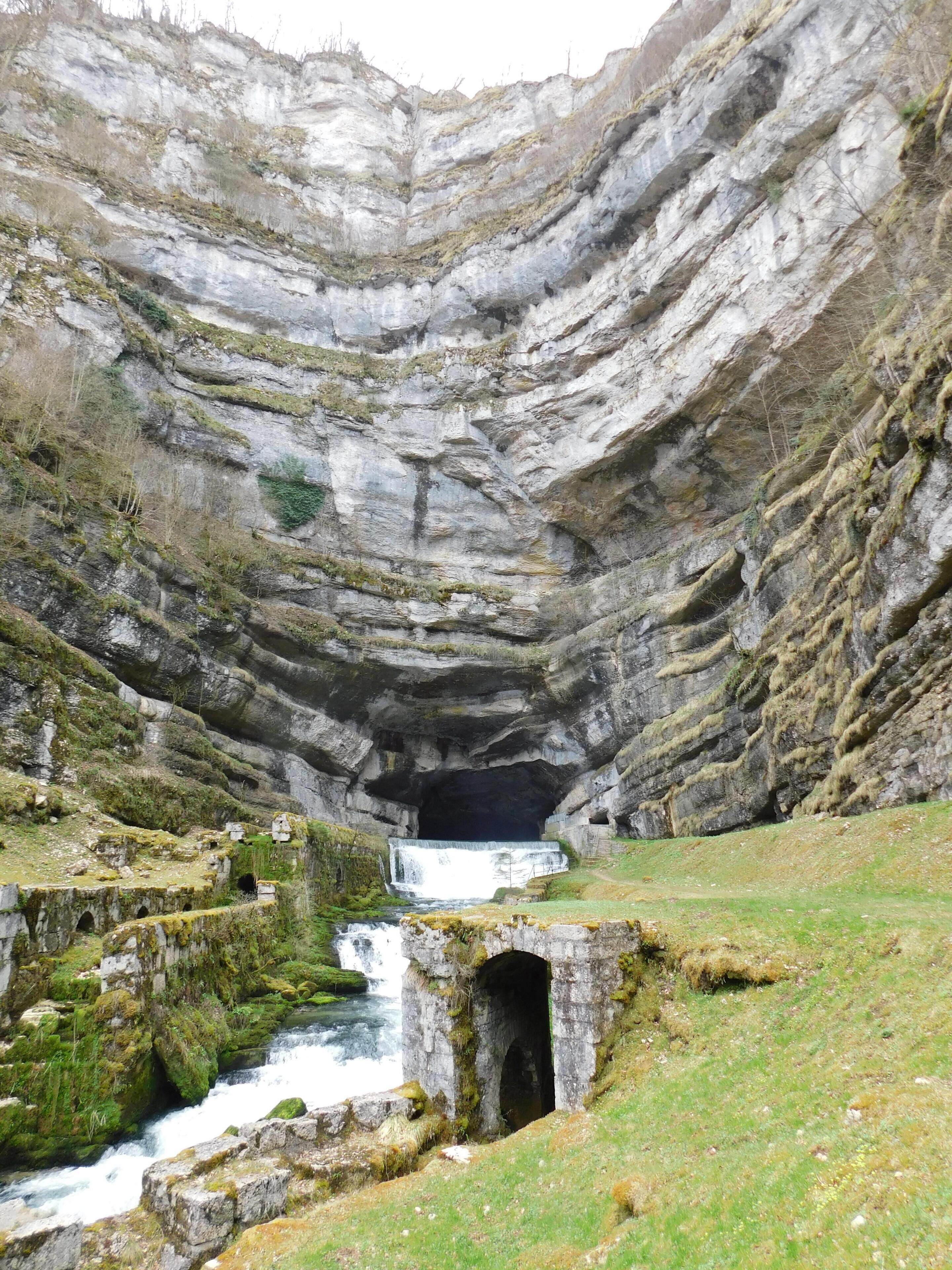 Eine natürliche Felsformation mit Wasserfall und einem kleinen Höhleneingang.