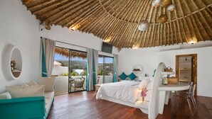 A bedroom with a large bed, a desk, a chair, a sofa, and a balcony with a view.