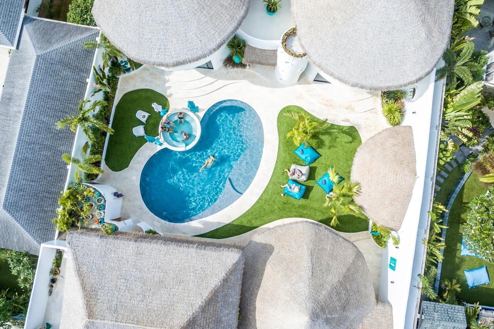 Vista aérea de un complejo turístico con piscina central, zonas de descanso y exuberante paisaje tropical.