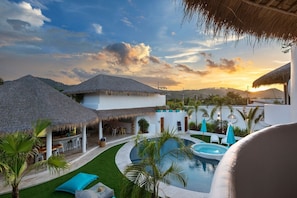 Ein Resort mit strohgedeckten Gebäuden, einem Swimmingpool und Blick auf den Sonnenuntergang.