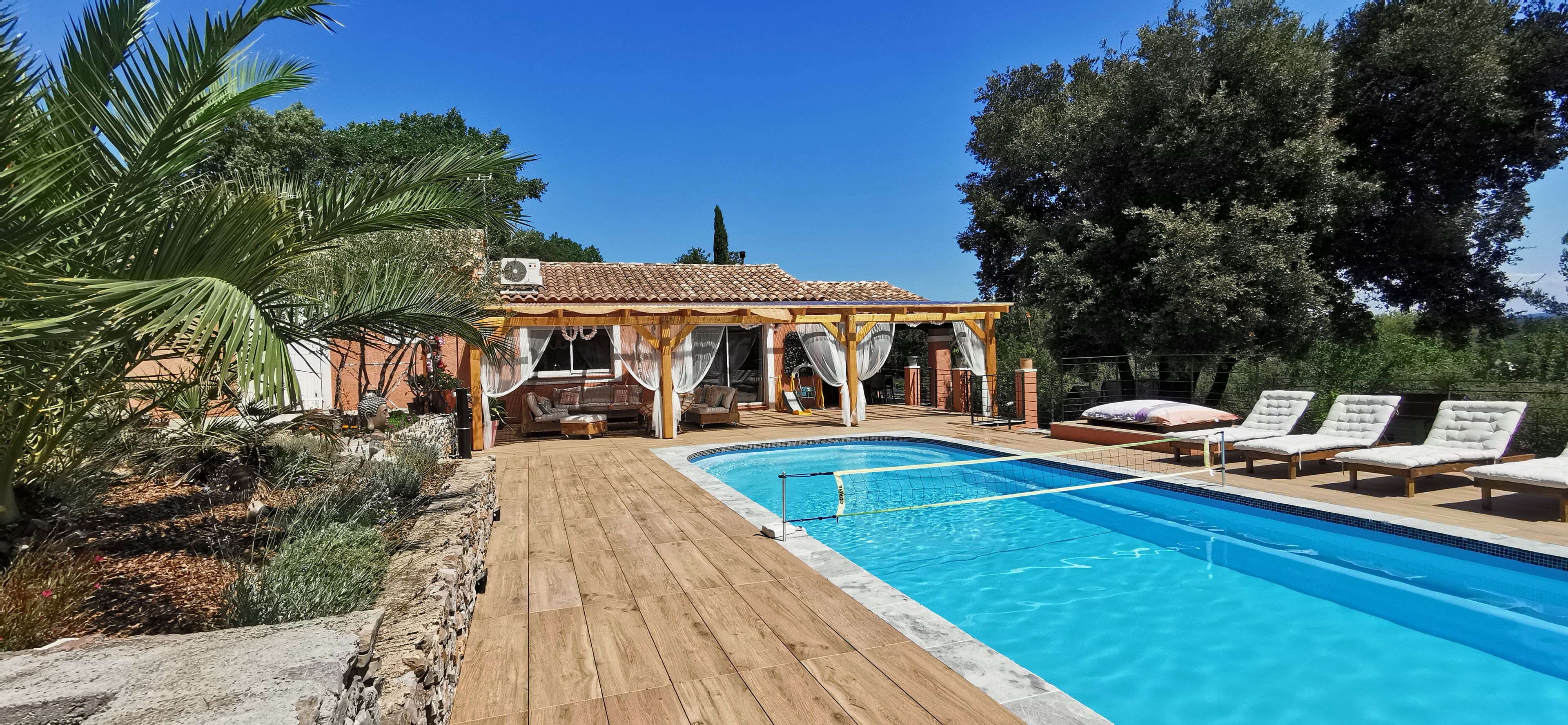 Un espace aménagé au bord de la piscine, comprenant un coin salon couvert, des chaises longues et une terrasse en bois.