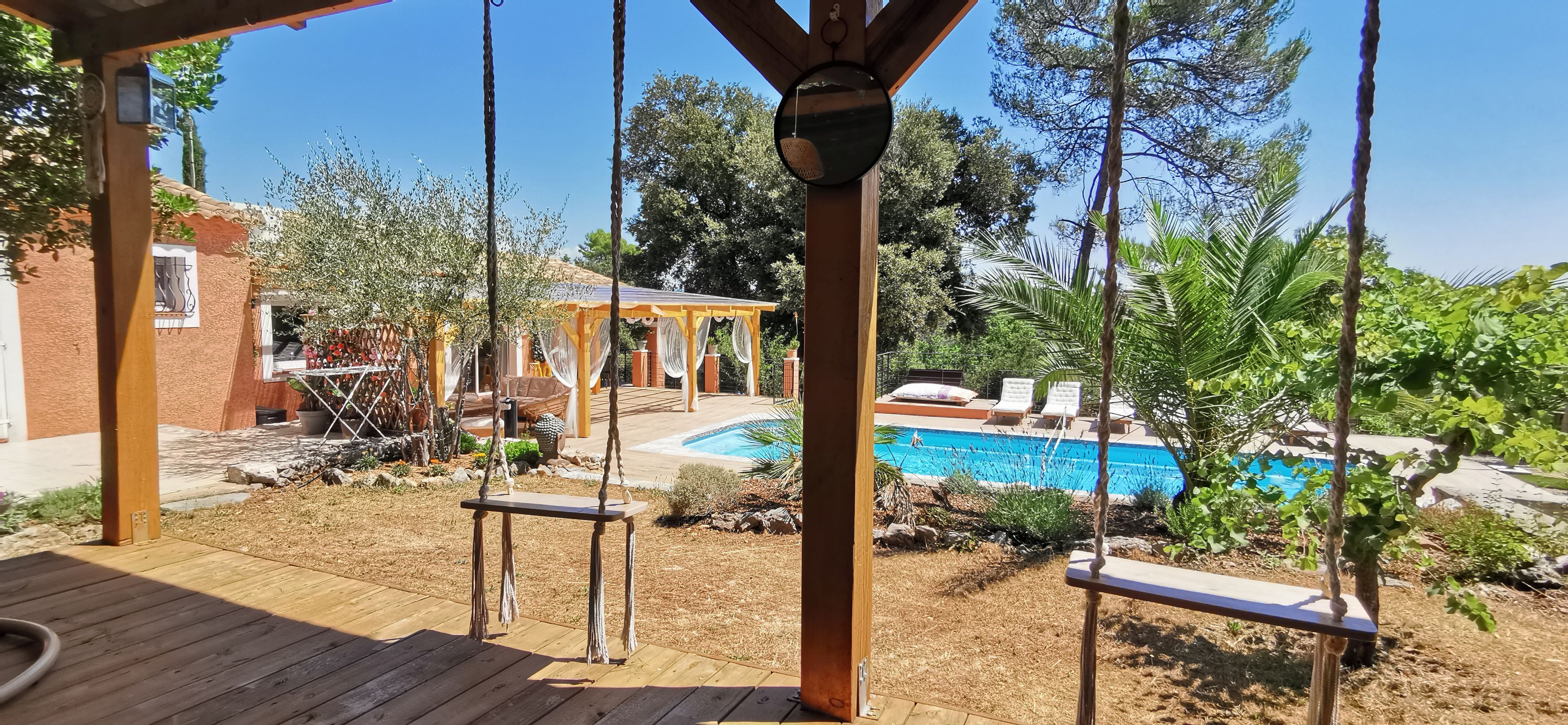 Eine Holzterrasse mit Schaukeln, einem Pool und einer überdachten Terrasse.