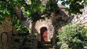A stone building with a central arched doorway, surrounded by greenery and climbing plants. - House, St Rome de Cernon (St Rome de Cernon)
