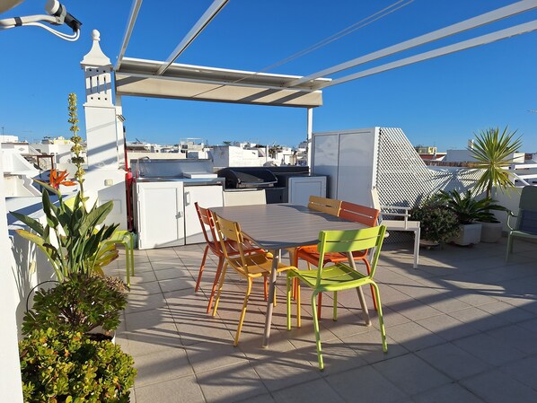 A rooftop terrace with a dining table, chairs, a grill, and potted plants. - Historic Roof Top Olhão, 360° panoramic sea view. (Olhão)