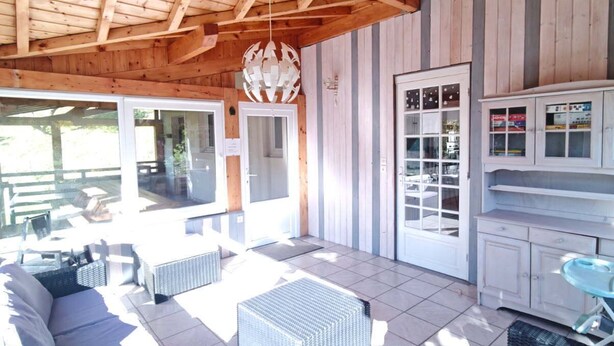 A covered outdoor seating area with wicker furniture, a tiled floor, and a wooden ceiling.
