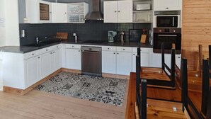 A modern kitchen with white cabinets, a black countertop, a stainless steel dishwasher, and a wooden dining table with chairs.